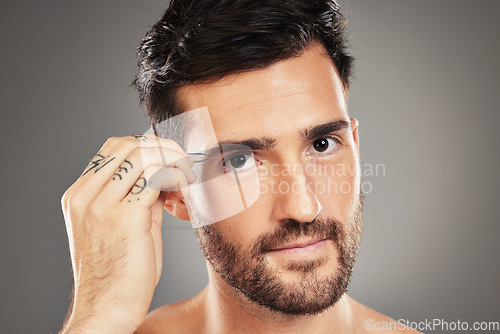 Image of Face, portrait and tweezers with a man model plucking his eyebrows in studio on a gray background. Skincare, wellness and luxury with a handsome young male tweezing his eyebrow hair for grooming