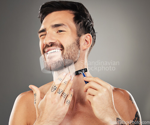 Image of Beard, smile and man shaving face for clean, healthy and beauty skin against grey studio background. Wellness, skincare and happy young cosmetic model with a razor to shave facial hair for grooming