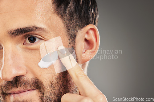 Image of Face, skincare and beauty with a man model using treatment in studio on a gray background for wellness. Finger, cosmetics and antiaging with a handsome young male inside to apply lotion to his cheek