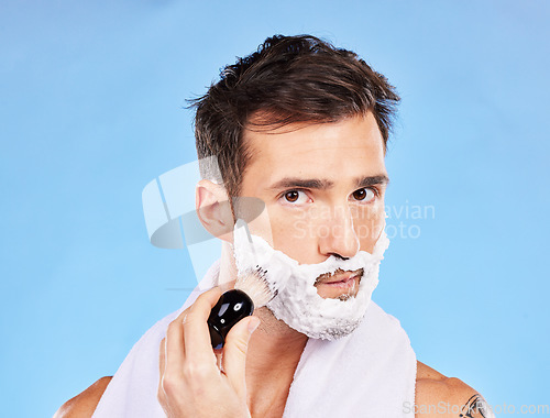 Image of Face, shave and grooming with a man model shaving his skin for hair removal in studio on blue background. Portrait, brush and hygiene with a handsome young male in the bathroom for a morning routine