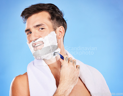 Image of Face, shave and hair removal with a man model shaving his skin in studio on a blue background for wellness or hygiene. Portrait, beard and razor with a young male grooming alone in the bathroom