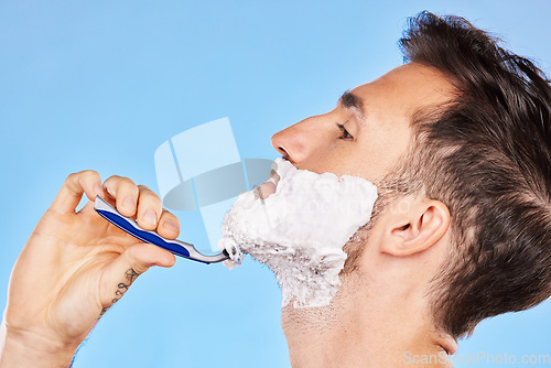 Image of Shave, cream and man grooming his beard with a shaver in studio for health, skincare and hygiene. Foam, razor and model shaving his facial hair for a face or skin routine isolated by blue background.