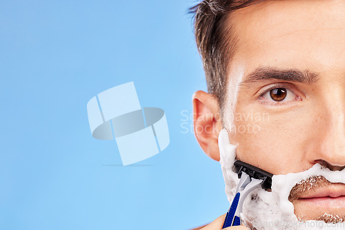 Image of Face, shave and grooming with a man model shaving his beard in studio on a blue background with mockup. Portrait, closeup and razor with a handsome young male in the bathroom for hair removal