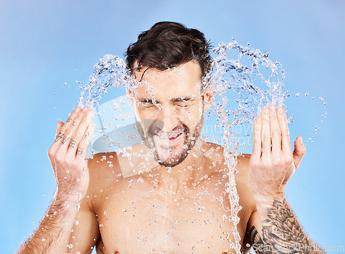 Image of Face, water and cleaning with a man model splash in studio on a blue background for hygiene. Skincare, water splash and hydrate with a handsome young male washing his skin in the bathroom for care