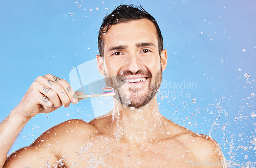 Image of Shower, brushing teeth and hygiene with a man model in studio on a blue background with splash for oral care. Water, cleaning and dental with a handsome young male wet in the bathroom for wellness