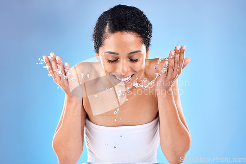 Image of Black woman, cleaning face with water, skincare and wellness with smile against a mockup studio blue background. Female model washing face, beauty and happy for skin health, happiness or water splash