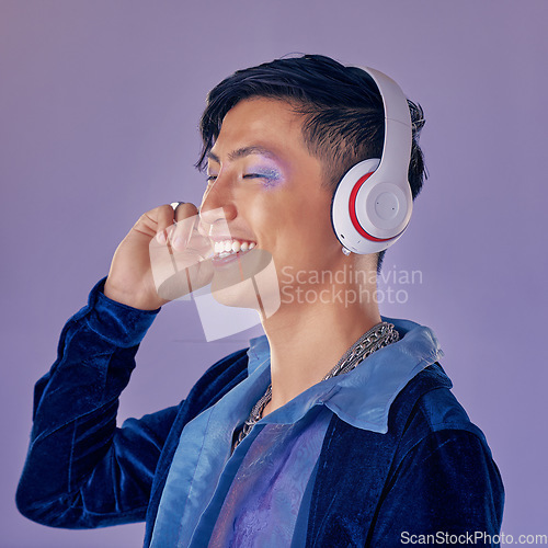Image of Music, makeup and cyberpunk with an asian man model in studio on a purple background for lgbt freedom. Future, happy and fashion with a handsome young androgynous male streaming or listening to audio