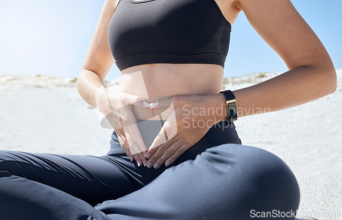Image of Weightloss, hands and heart shape on a stomach after workout in nature at the beach for wellness. Health, fitness and girl athlete with self love gesture by tummy at outdoor yoga, pilates or exercise