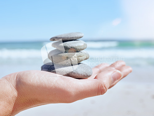 Image of Hand, stones pile and beach with a woman holding little rocks by the ocean for balance, wellness or zen. Nature, earth and mindfulness with a rock stock in the palm of a female on the sand by the sea