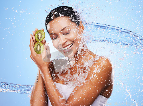 Image of Water splash, kiwi and skincare of woman in studio isolated on a blue background. Healthcare, wellness and hygiene of female model from India with fresh and clean fruit for antioxidants or vitamin c.