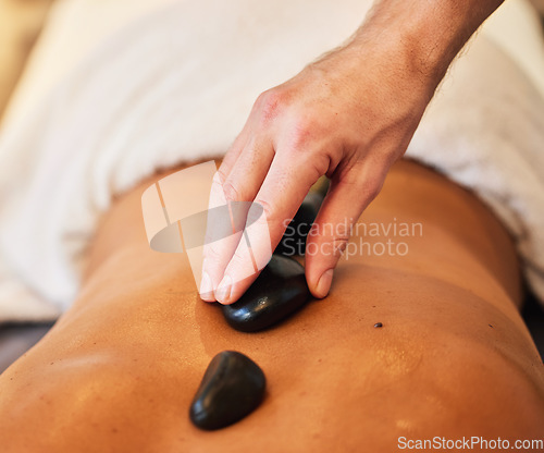 Image of Hands, back and rock massage at spa for stress relief, relaxation and spiritual zen treatment at a resort. Hand of therapist applying hot rocks or stone to skin for body care, healing or wellness