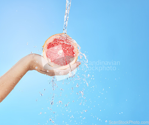 Image of Hand, grapefruit and water splash for skincare nutrition, wellness or cosmetics against a blue studio background. Person hold citrus fruit in healthy, hydration or hygiene for natural vitamin C skin