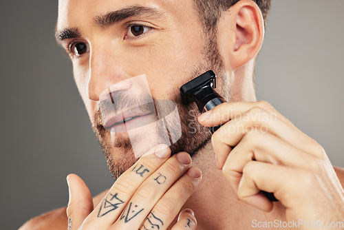 Image of Shaver, beard and man grooming in a studio for beauty, hygiene and skincare for wellness. Health, shave and healthy guy shaving his facial hair with a cosmetic razor isolated by a gray background.