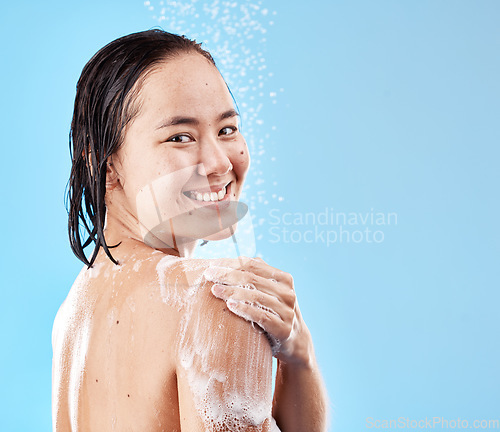 Image of Shower, woman and hygiene for wellness, smile and happy with cleaning, water and soap against blue studio background. Portrait, young female and lady doing scrub, washing and health with happiness.