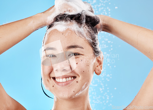 Image of Woman, shampoo and shower in studio portrait with hair care, cleaning and smile by blue background. Model, hair and wellness with foam, soap or water for self care, cosmetics or beauty with happiness