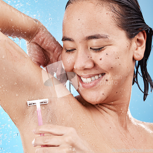 Image of Shower, woman shave armpit with razor and clean beauty with water and hygiene for grooming against blue studio background. Happy Asian model, healthy skin and wet with hair removal and shaving.