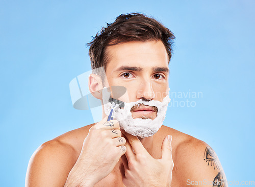 Image of Portrait, shave and razor with a man model grooming in studio on a blue background for wellness or care. Face, skin and shaving with a handsome young male in the bathroom for facial hair removal