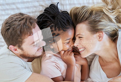 Image of Family, interracial and love, happy and together with adoption or foster care overhead and bonding together in family home. Happy family lying on bed, cuddle and smile with mother, father and child.