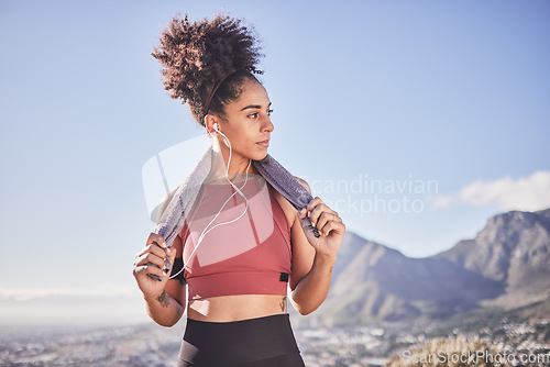 Image of Fitness, towel and black woman with earphones in nature after running, workout or training. Health, wellness or female streaming music, radio or podcast, audio or song on break after exercising alone