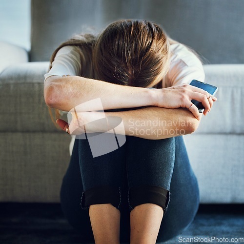 Image of Sad, depression and woman with phone in living room home after break up message, cyber bullying victim or grief. Mental health, anxiety or depressed female holding 5g mobile smartphone alone in house