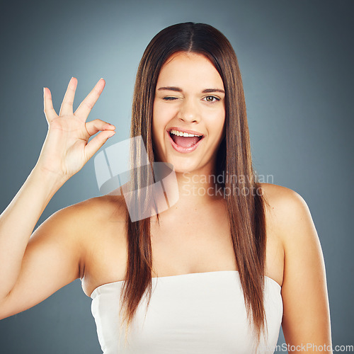 Image of Hand sign, perfect and wink with a model woman in studio on a blue background for skin or hair care. Portrait, face and solan with an attractive young female using a gesture to show satisfaction