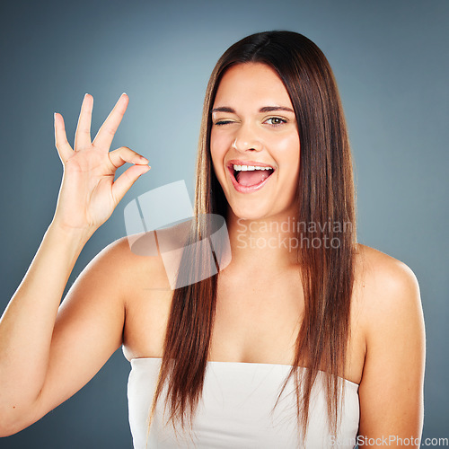 Image of Ok hand sign, woman and happy for success with face wink or advertising marketing in studio. Influencer approval, beauty cosmetics and campaign approval, yes or good job against blue wall background