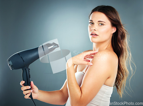 Image of Beauty, haircare and hairdryer with a model woman in studio on a blue background drying her hair with an appliance. Wellness, salon and luxury with an attractive young female blowdrying her hairstyle