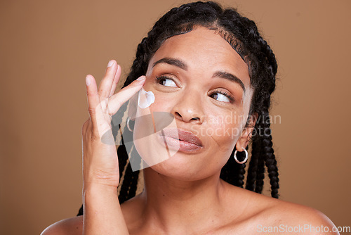 Image of Black woman, skincare and facial moisturizer for beauty cream, makeup or cosmetics against a brown studio background. African American female applying lotion to smooth or hydrate skin for treatment