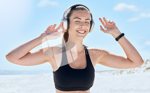 Image of Music, headphones and woman listening during fitness outdoor, podcast or audio streaming with smile and enjoy workout. Exercise at the beach, wellness and listen to radio with energy and freedom.