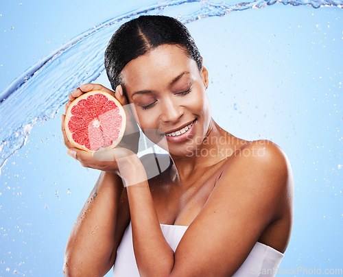Image of Grapefruit, black woman and water splash, beauty and skincare, vitamin c and healthy natural cosmetics of body wellness on studio blue background. Happy african model, wet citrus fruits and nutrition