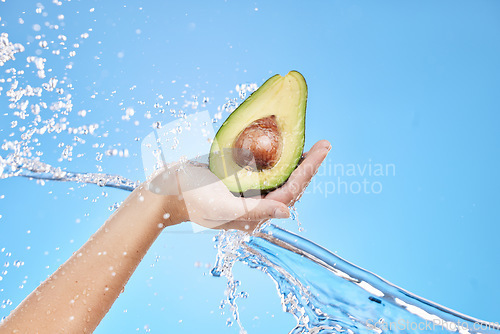 Image of Hand, water and avocado for beauty splash and organic skincare product on a blue studio background. Avo, vegetable and natural produce for bodycare, skin care and nutrition or healthy diet