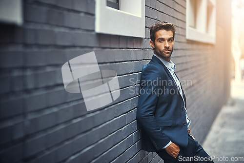 Image of Fashion, suit and city with a business man or model leaning against a brick wall outdoor for contemporary style. Corporate, executive and trendy with an edgy male posing in the alley of an urban town