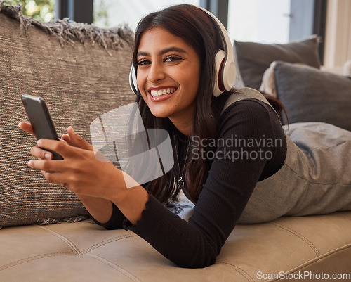 Image of Woman, smile and phone listening to music with headset while relaxing on living room sofa. Portrait of happy female in relax and enjoying audio track, chatting or texting on smartphone on the couch