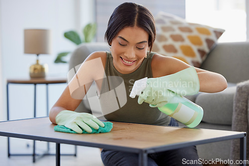 Image of Woman, detergent and smile for cleaning table, hygiene or sanitary wiping in the living room at home. Female spraying anti bacterial liquid cleaner on wooden desk for health safety and hygienic house