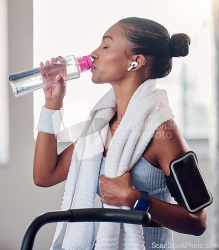 Image of Drinking water, fitness and smartphone on woman arm gym gear, technology and listening to music for workout on stationary cycling machine. Tired, challenge and motivation black woman cardio training