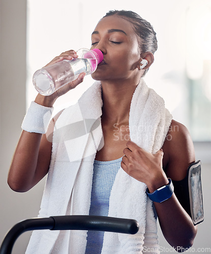 Image of Fitness, health and woman drinking water in gym, rest and drinking while listening to music streaming app. Training, exercise and water, girl stop on treadmill or exercise bike, relax during workout.