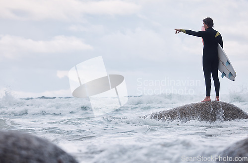 Image of Man, pointing or surfer on rocks at beach, ocean or rough sea and watching tide, waves or water movement in Hawaii. Sports athlete, surf board or surfing person in fitness, workout or nature training