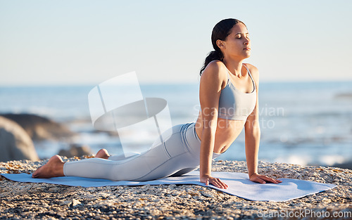 Image of Yoga, fitness and woman at the beach for exercise while in cobra pose for breathing, zen and wellness on rock while on vacation in summer. Female by sea to meditate, workout and practice mindfulness