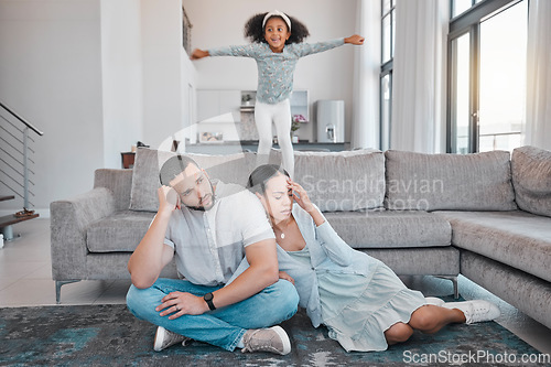 Image of Tired, parents and child jump on sofa with exhausted mother and father sitting on floor in living room. Family, energy and young girl jumping on couch with frustrated, annoyed and upset mom and dad