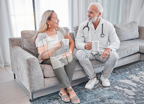 Image of Home visit, doctor and woman on sofa talking and drinking coffee in living room after consulting. Healthcare, medicine and a medical professional man and lady on couch in house or apartment with tea.