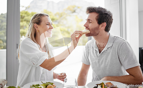 Image of Couple, food and eating lunch with a woman feeding her man on a romantic date at home at the dining table. Health, nutrition and diet with a husband and wife eating delicious meal or lunch