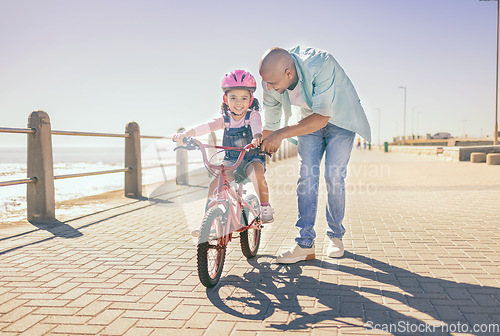 Image of Father, child and bicycle with a girl learning to ride a bike on promenade by sea for fun, bonding and quality time on summer vacation. Man teaching his daughter or girl safety while cycling outdoor