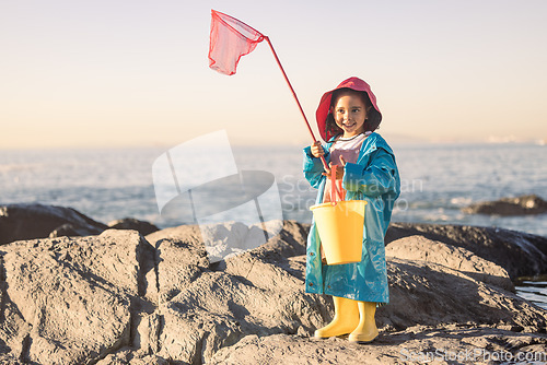 Image of Child, girl or kid fishing net or bucket by beach rock pools, ocean or sea for salt water shrimp, muscles or crabs on summer holiday. Smile, happy or youth and fisherman equipment in Brazilian nature