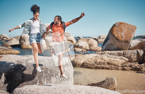 Image of Black couple, fitness and beach while on vacation taking a jump or leap from a rock for travel, adventure and exercise in summer. Happy man and woman together at sea for quality time on holiday