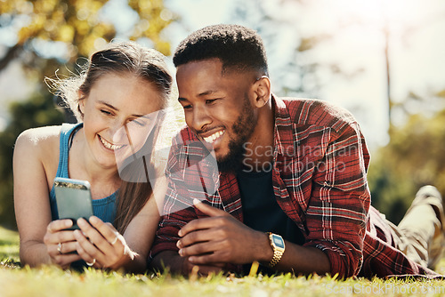 Image of Interracial, couple and phone social media in park to relax, bond and smile together in Los Angeles. Technology, streaming and happy people enjoy summer in nature with mobile app entertainment.