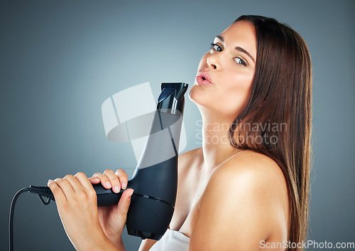 Image of Beauty, hair dryer and care with a model woman in studio on a blue background to promote haircare. Face, portrait and hair care with an attractive young female holding a blow drying appliance
