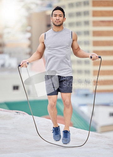 Image of Jump, rope and man on a rooftop for fitness training, exercise and skipping for cardio in the city. Jumping, focus and Asian athlete with energy for an urban workout for wellness, body and health