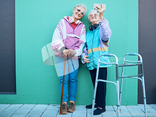 Image of Phone, selfie and disability with senior friends posing for a photograph outdoor on a green wall background. Happy, mobile and walker with a mature woman and friend taking a picture together