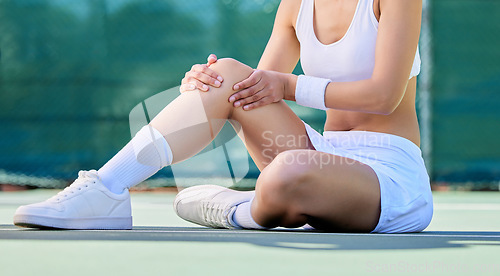 Image of Tennis, knee and injury with a sports woman holding her joint in pain while sitting on a tennis court. Fitness, exercise and workout with a female tennis player suffering with muscle cramp or strain