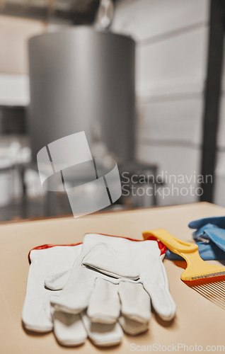 Image of Gloves, beekeeping and production with equipment in an empty factory, plant or warehouse for honey extract. Farm, agriculture and sustainability with protective workwear on a table for manufacturing